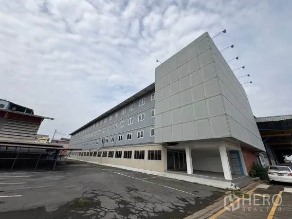 Factory for rent in Phra Pradaeng, Samut Prakan - Angled view of modern office façade beside the warehouse with ample driveway and parking.