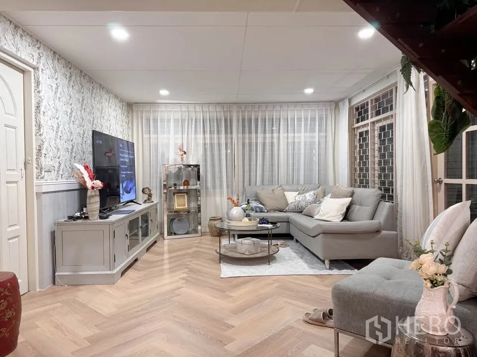 Detached House for rent in Huai Khwang, Bangkok - Bright living room with L-shaped sofa, TV console and herringbone wood floor.