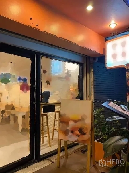 อาคารพาณิชย์ ให้เช่าในPhaya Thai, Bangkok - บรรยากาศค่ำของหน้าร้าน ใต้กันสาดสีส้ม พร้อมประตูกระจก ป้ายไฟ และกระถางต้นไม้.
