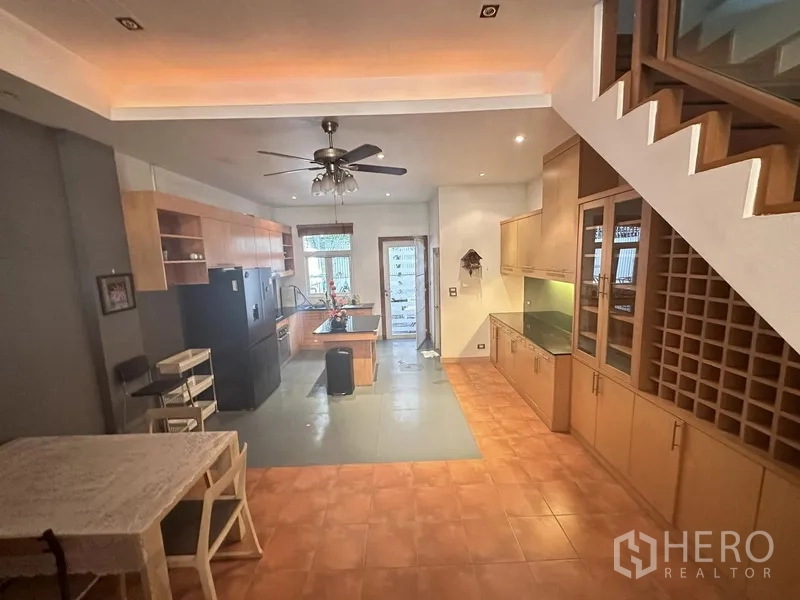 Townhouse for rent or sale in Khlong Toei, Bangkok - Wide view of kitchen–dining area under the stairs with built-in cabinets and wine rack.