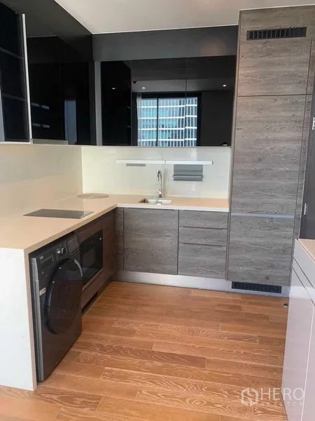 Condominium for rent in Pathum Wan, Bangkok - Sleek L‑shaped kitchen with induction hob, built‑in appliances and washer‑dryer in Lumphini condo.