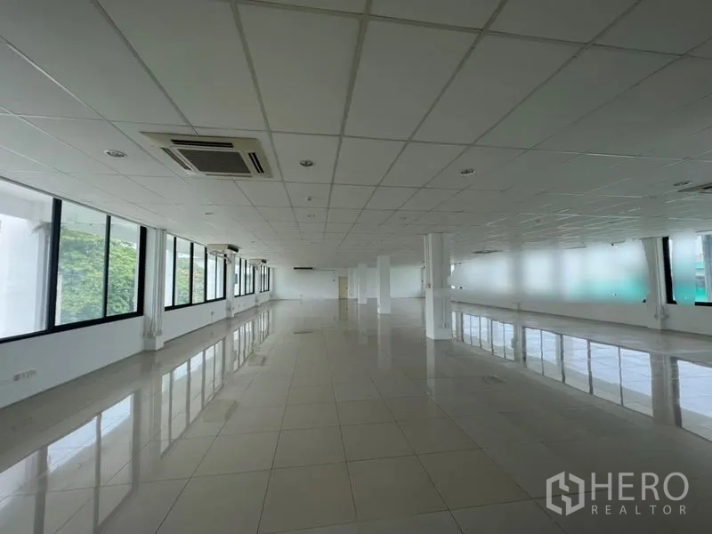 Office Space for rent - Extended open workspace with cassette AC units, support columns and wide windows overlooking greenery.