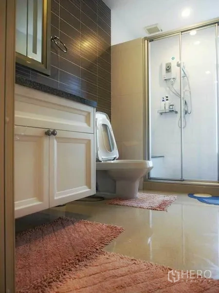 Detached House for rent or sale in Pak Kret, Nonthaburi - Modern bathroom featuring a glass-enclosed shower, white vanity, toilet and brown tiled accent wall.