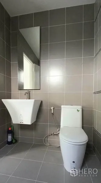 Townhouse for sale in Mueang Pathum Thani, Pathum Thani - Modern bathroom with gray tiles, wall-mounted sink, mirror, and toilet with bidet spray.