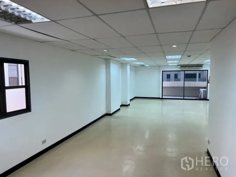 Office Space for rent in Pathum Wan, Bangkok - Bright open-plan office interior with white walls, drop ceiling, fluorescent lights, window and sliding glass doors.