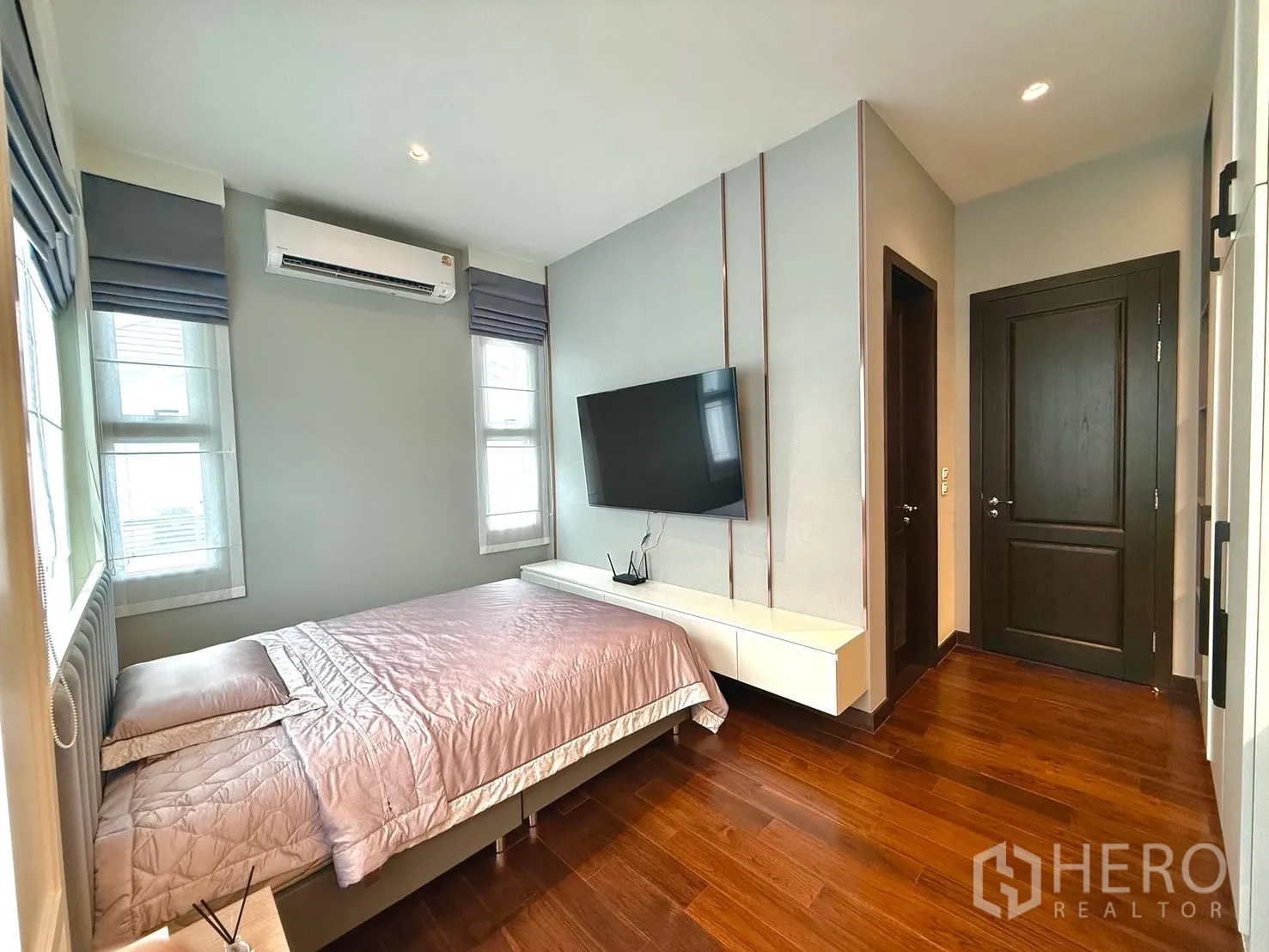 Detached House for rent or sale in Bang Phli, Samut Prakan - Secondary bedroom with wall-mounted TV, air conditioner, built-in console and wooden floor.