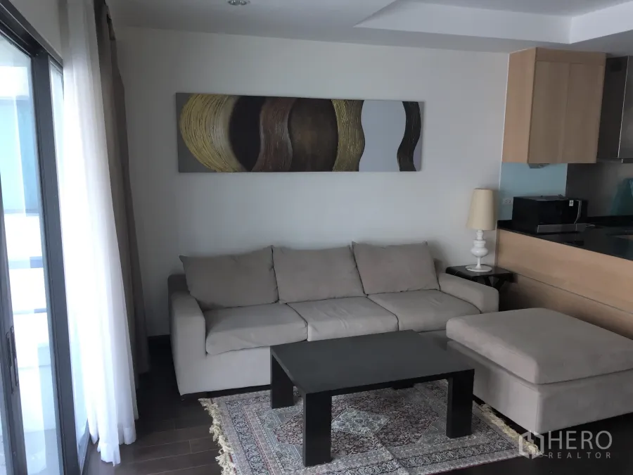 Condominium for rent in Sathon, Bangkok - Bright living room with beige sofa, abstract wall art, coffee table and sliding door to the balcony.