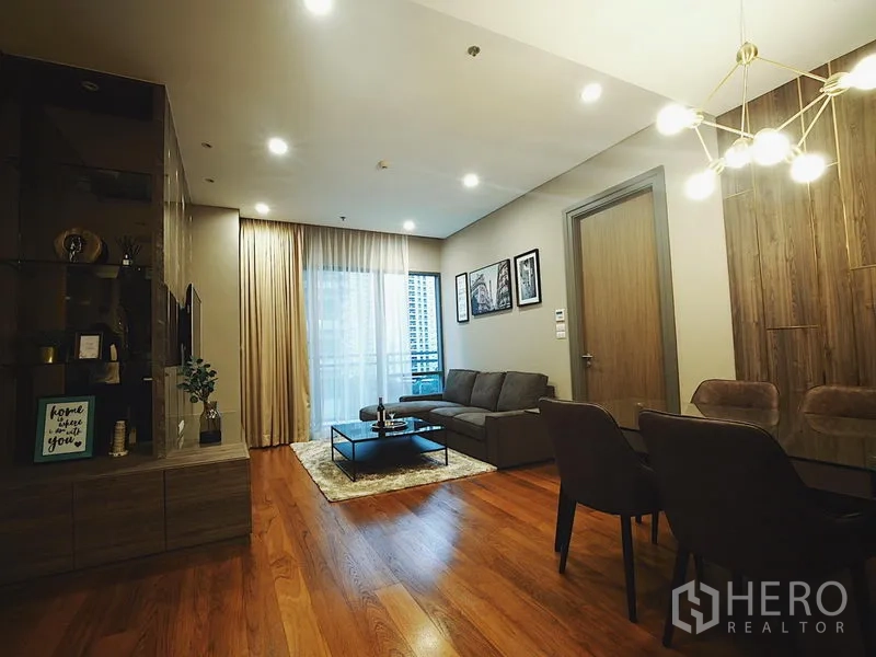 Condominium for rent in Khlong Toei, Bangkok - Modern living and dining room with sofa, TV wall, chandelier and balcony window.