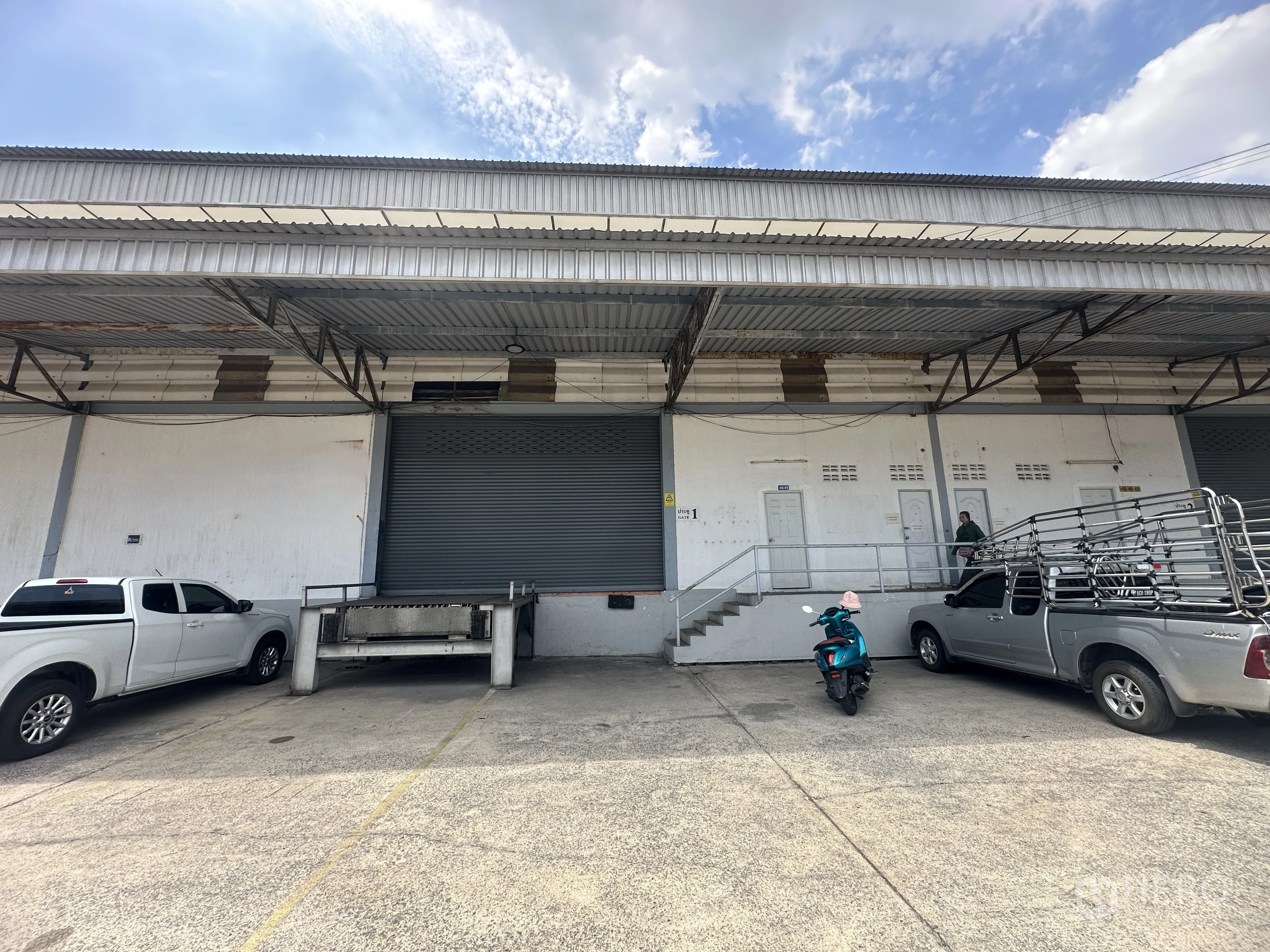Warehouse for rent in Khlong Luang, Pathum Thani - Multiple dock-high bays with stairs, roller doors, and vehicles parked in front.