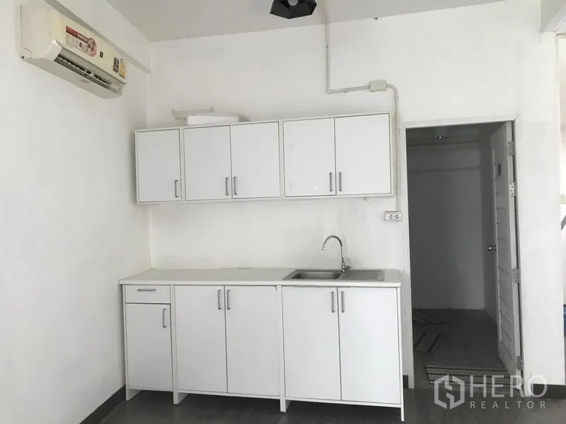 Shophouse for rent in Watthana, Bangkok - Pantry wall with overhead cabinets, sink and AC unit next to a doorway to the wet area.