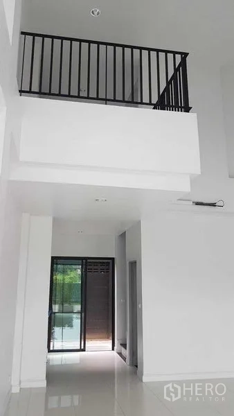 Shophouse for rent or sale in Bang Na, Bangkok - Bright double-height lobby with white walls, glossy floor and black metal mezzanine railing.
