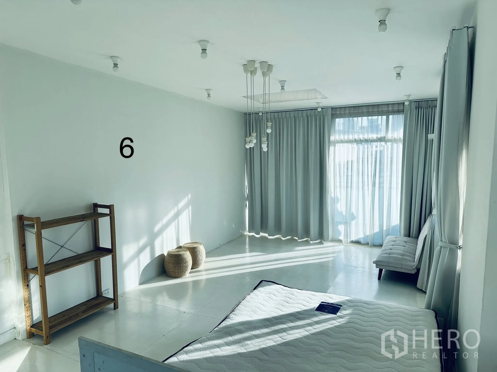 Shophouse for rent in Watthana, Bangkok - Bright upper-floor room with large curtained windows, pendant bulbs, a wood shelf, and a mattress.