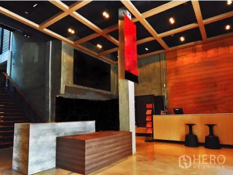 Shophouse for rent in Suan Luang, Bangkok - Loft-style reception of a shophouse with concrete walls, timber ceiling grid, red hanging sign, staircase, and long counters.