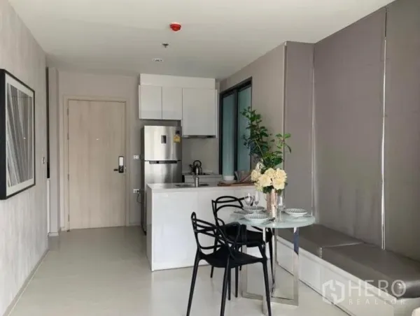 Condominium for rent in Khlong Toei, Bangkok - Compact modern kitchen with refrigerator, sink island, and small dining table beside large windows.