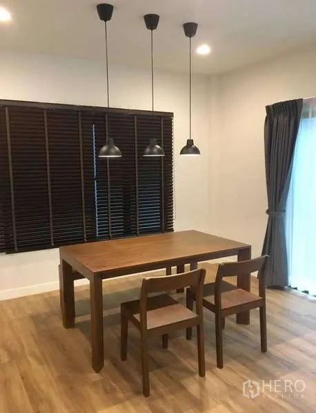 Detached House for rent in Bang Kapi, Bangkok - Dining area with wooden table, three pendant lights and dark window blinds.