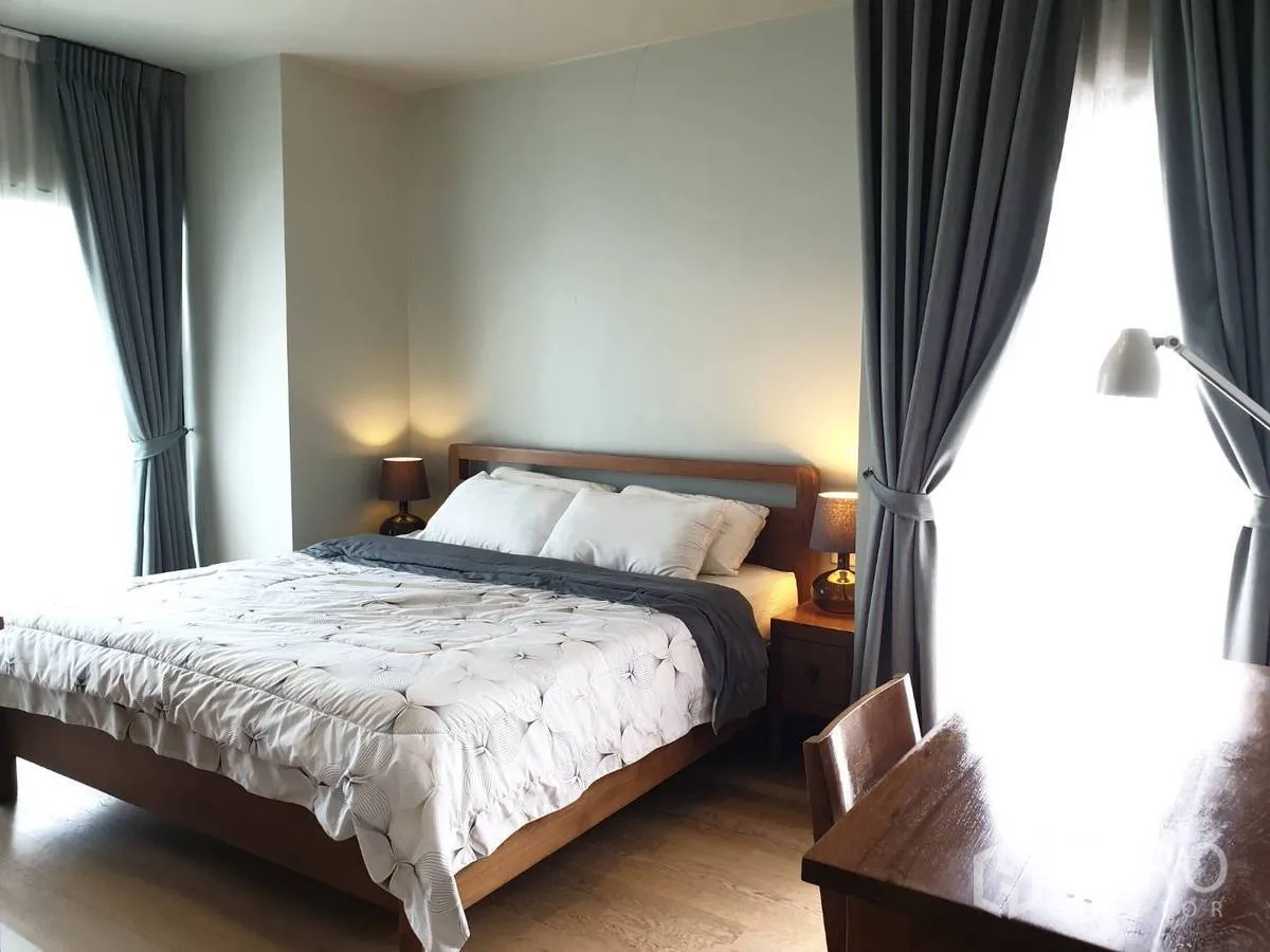Condominium for rent or sale in Bangkok - Primary bedroom with king bed, bedside tables and study desk by full-height windows.