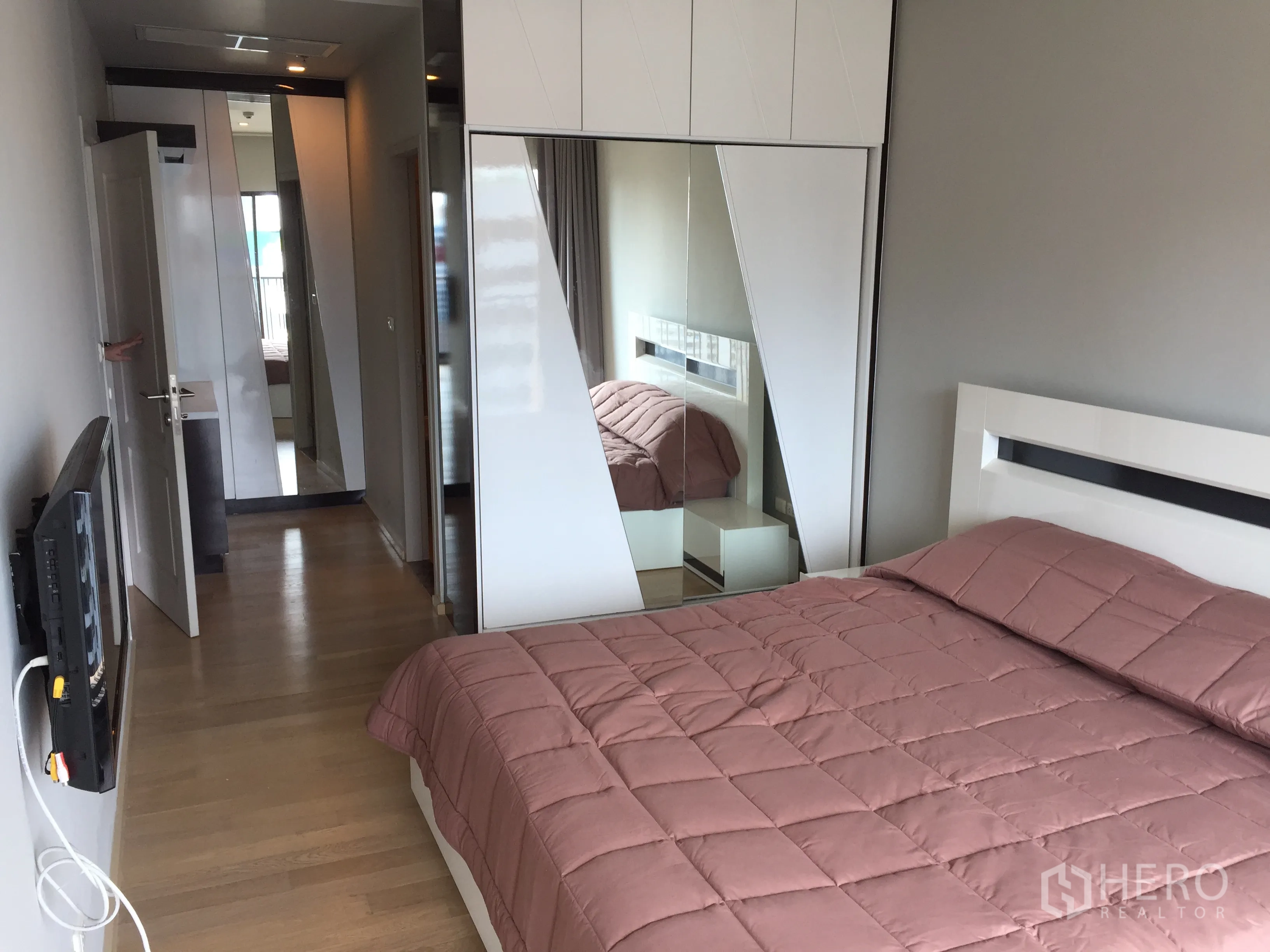 Condominium for rent in Bangkok - Bedroom featuring built-in mirrored wardrobe, wall-mounted TV and warm wood flooring.