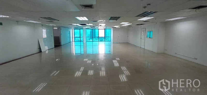 Office Space for rent in Huai Khwang, Bangkok - Wide unfurnished office floor with many ceiling light panels and windows at the far end.