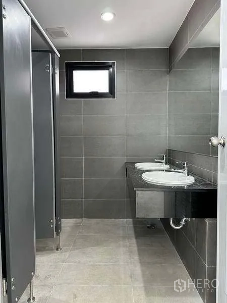Factory for rent in Bang Phli, Samut Prakan - Restroom with gray tiles, toilet cubicles and twin sinks in the factory office.