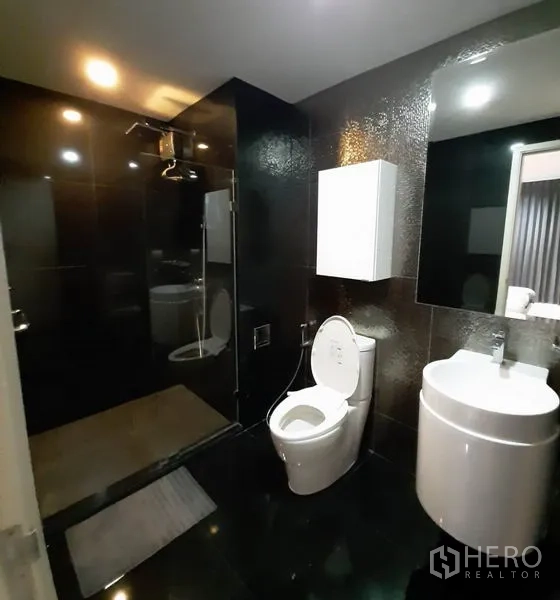 Condominium for rent or sale in Khlong Toei, Bangkok - Contemporary bathroom with glossy black tiles, walk-in glass shower, round basin and toilet.