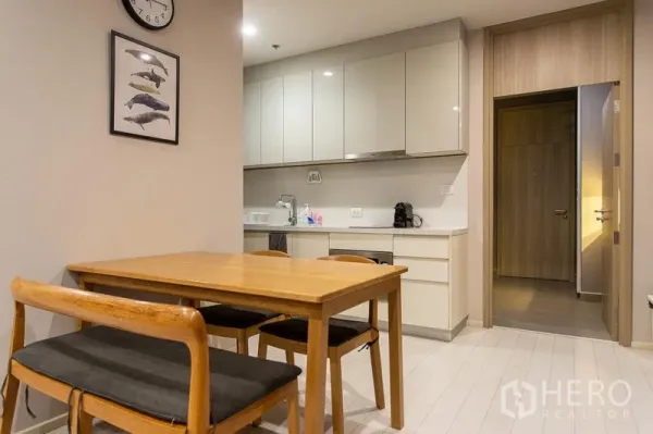 Condominium for rent in Pathum Wan, Bangkok - Dining area with wooden table and chairs beside a compact kitchenette in a Pathum Wan condo