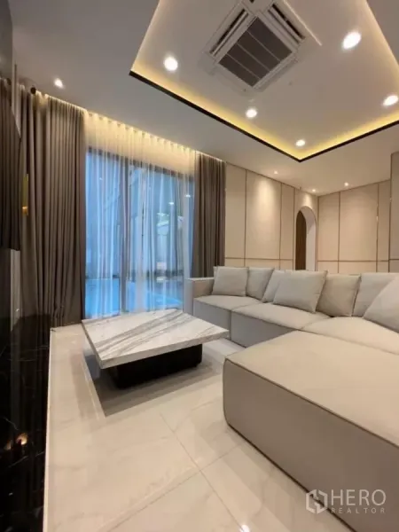 Detached House for rent in Phaya Thai, Bangkok - Lounge with large sectional sofa, marble coffee table and pool view through curtains.
