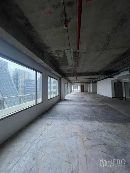 Office Space for rent in Watthana, Bangkok - Long shell-and-core office floor with exposed concrete ceiling and large windows overlooking the city.
