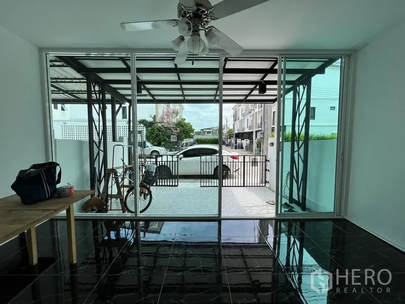 Townhouse for sale in Bang Kapi, Bangkok - Glass-enclosed front room with sliding doors opening to a covered carport.