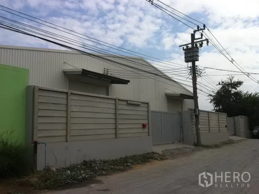 货栈 出租在Sai Mai, Bangkok - 赛迈区街景视角的仓库园区，高围墙与金属大门出入口，沿街电力线路可见。