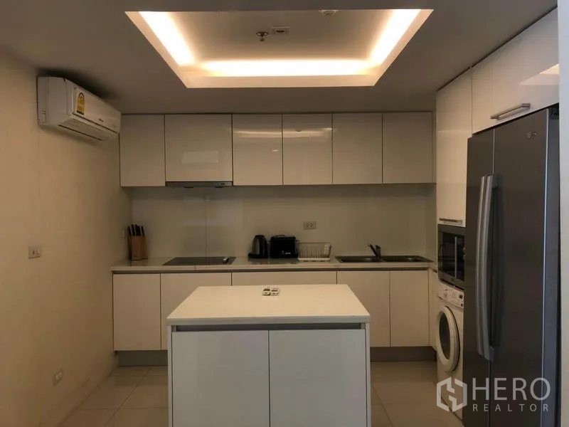 Condominium for rent in Pathum Wan, Bangkok - Modern white kitchen with island, full-height cabinets, fridge and washing machine.
