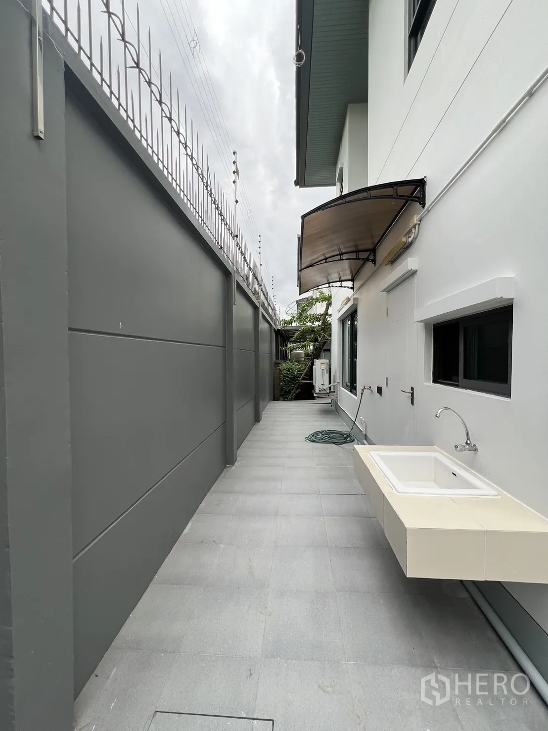 Detached House for rent in Bang Kapi, Bangkok - Rear utility area with outdoor sink, tiled floor and high privacy wall.