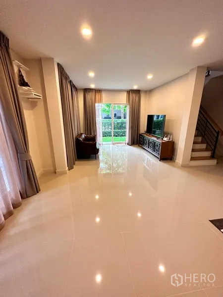 Detached House for sale in Prawet, Bangkok - Living room with glossy tile flooring, TV console and sliding doors to the garden.