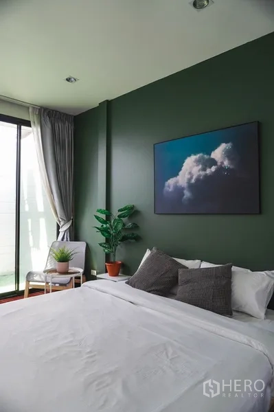 Townhouse for rent in Watthana, Bangkok - Bright master bedroom with green accent wall, sliding glass doors to the balcony and a cozy seating corner.