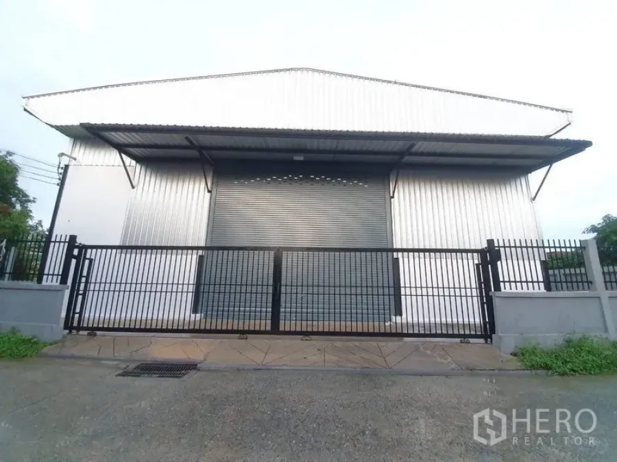 Warehouse for rent in Bang Khen, Bangkok - Front view of the warehouse showing wide roller shutter, roof awning and black metal fence.