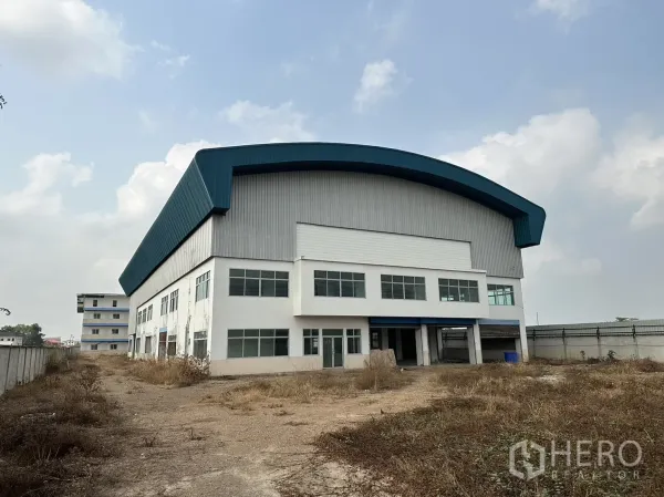 Factory for rent in Pak Kret, Nonthaburi - Large factory exterior showcasing curved blue roof and two‑storey office facade with multiple windows.