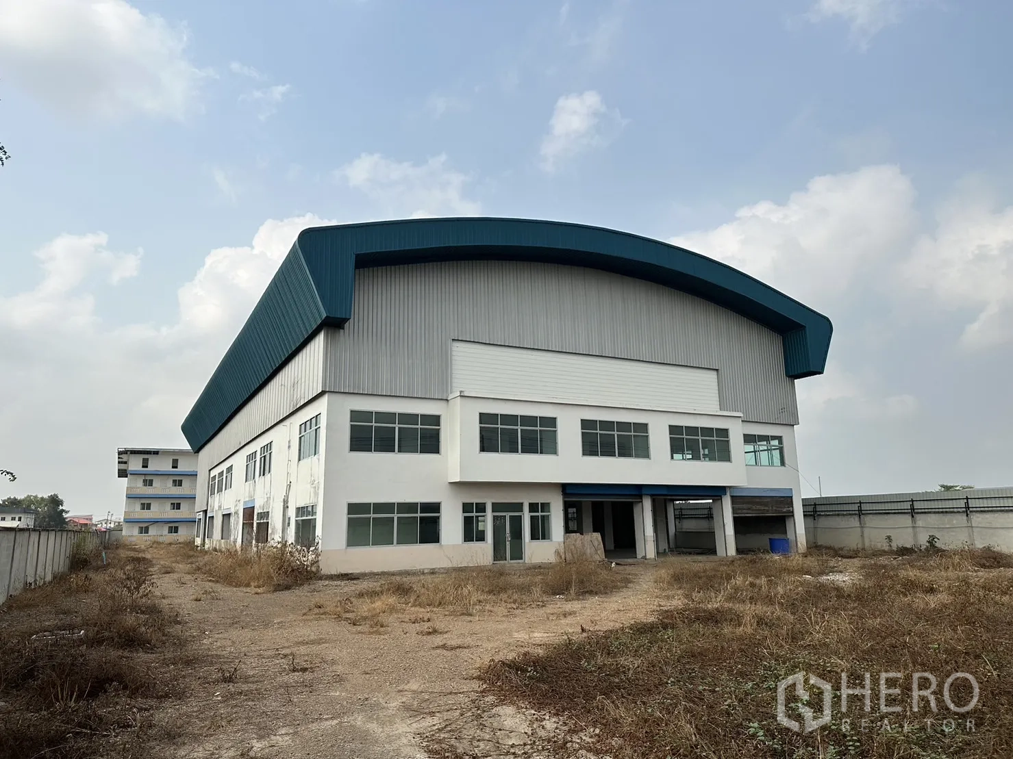 Factory for rent in Pak Kret, Nonthaburi - Large factory exterior showcasing curved blue roof and two‑storey office facade with multiple windows.
