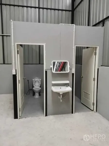Warehouse for rent in Chatuchak, Bangkok - On-site restrooms inside the warehouse featuring two cubicles with toilets and wall-mounted sinks.