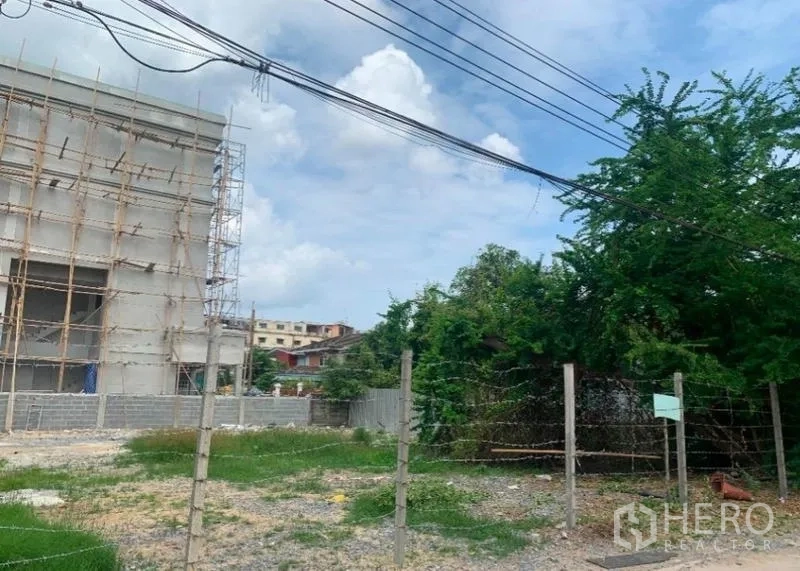 Land for rent in Khlong Toei, Bangkok - Open plot beside a low-rise building under construction, with boundary fencing and overhead utilities.