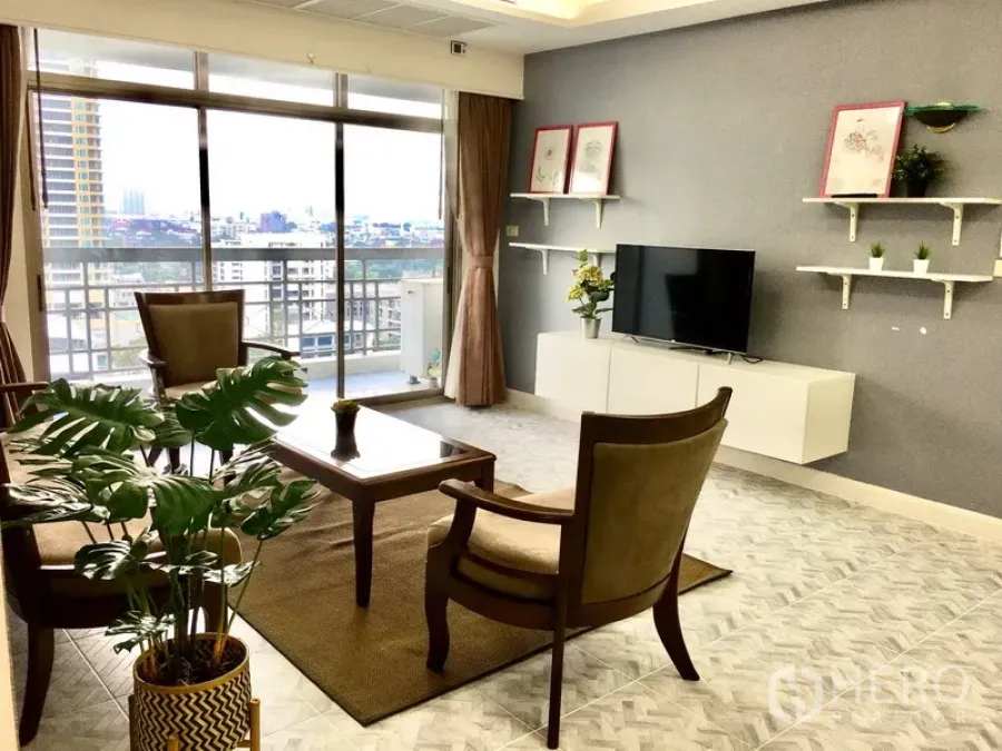 Condominium for rent or sale in Watthana, Bangkok - Bright living room with sliding glass doors to a balcony, city view, floating TV console and wall shelves.