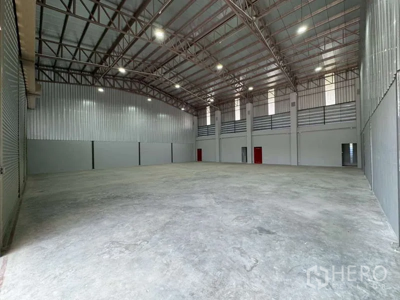 Warehouse for rent in Bang Phli, Samut Prakan - Expansive high-ceiling warehouse interior with LED lighting and red fire-exit doors