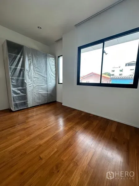 Detached House for rent in Watthana, Bangkok - Sunlit bedroom with warm wood flooring and a wrapped wardrobe by wide windows.
