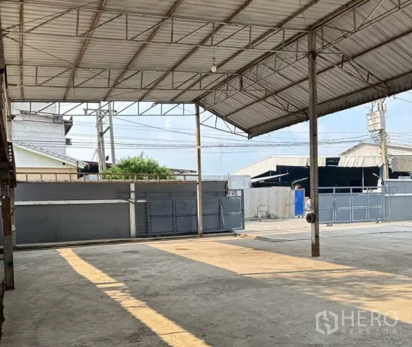 Factory for rent in Samut Prakan - Covered loading area with steel roof looking toward the gated entrance.