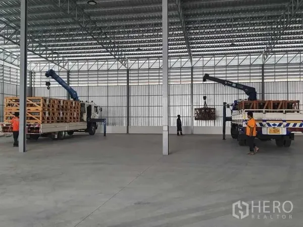 Warehouse for rent in Khlong Sam Wa, Bangkok - Trucks with loading cranes moving crated goods inside a large covered warehouse bay.