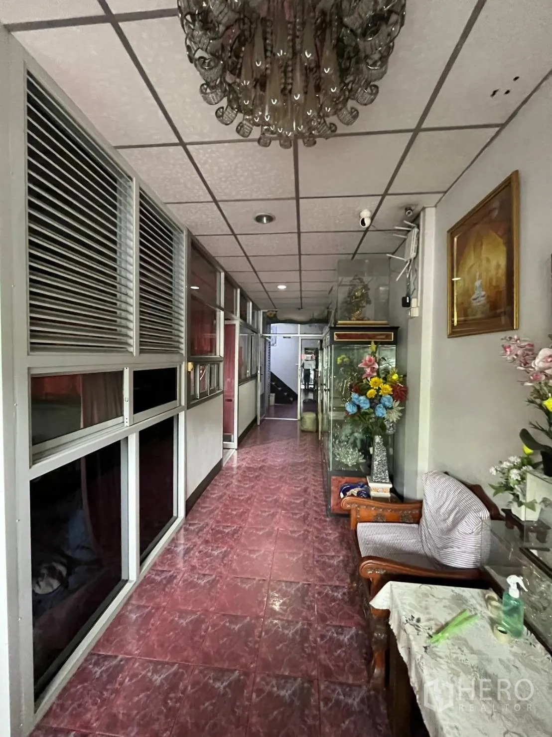 Shophouse for rent in Khlong Toei, Bangkok - Hallway with chandelier, glass display cabinets, seating, and red marble-style tiles.