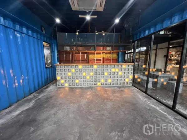 Retail Space for rent - Front view of lighted glass-block service counter against metal shelving in a container-style retail room.