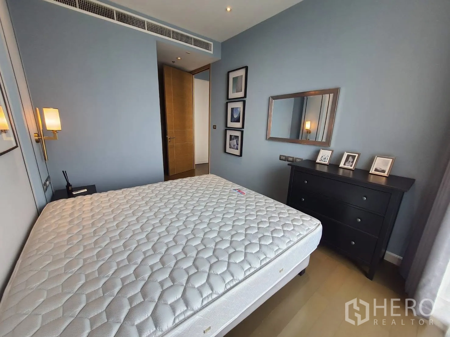 Condominium for rent in Pathum Wan, Bangkok - Bright bedroom with blue accent wall, wall sconces, large mirror and black dresser beside a queen mattress.