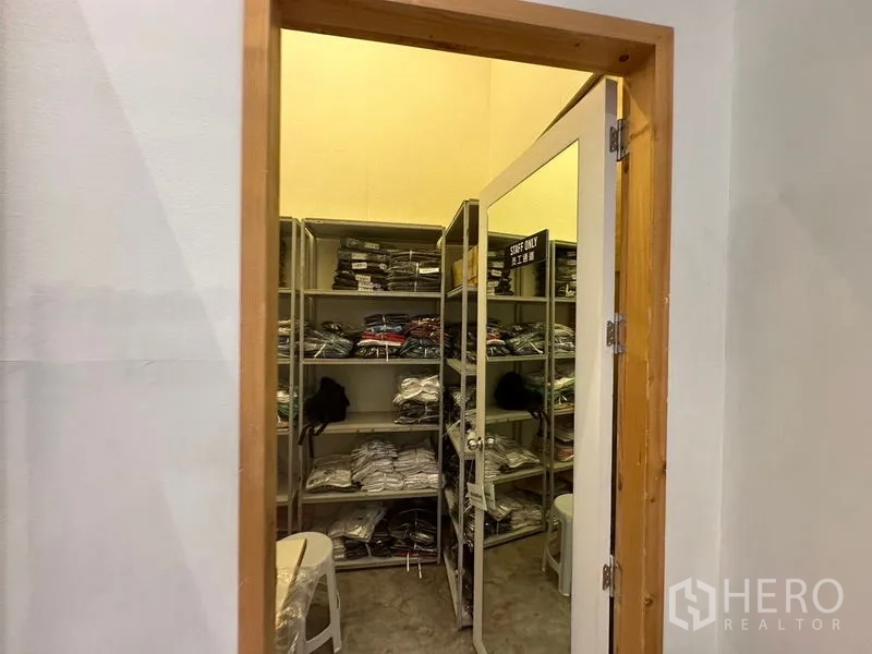 Retail Space for rent in Phra Khanong, Bangkok - Compact stock or fitting room with metal shelving and a mirrored door, organized merchandise.