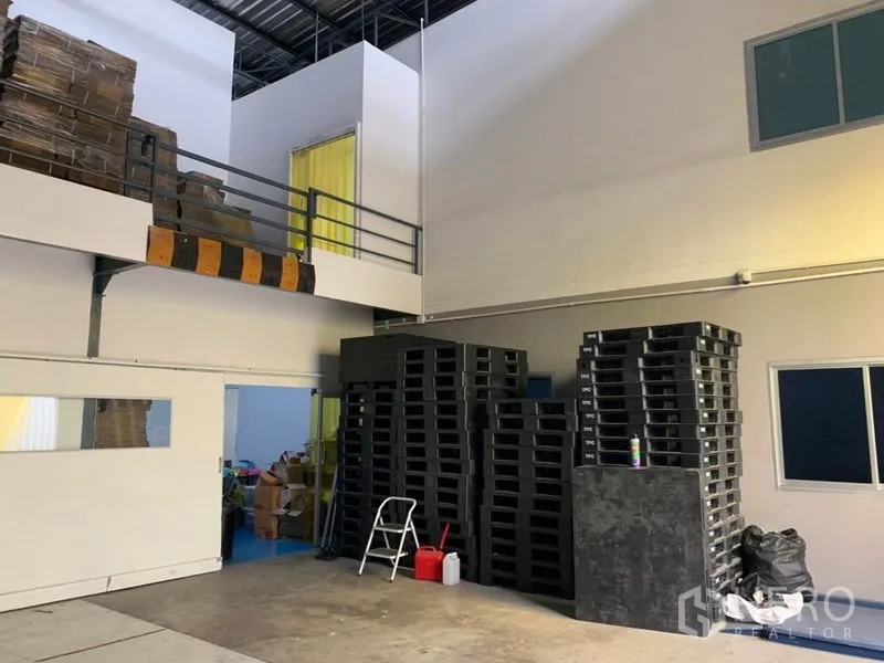 Warehouse for rent in Bang Kapi, Bangkok - Ground-floor loading area with stacked plastic pallets and enclosed mezzanine offices.
