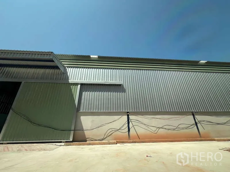 Warehouse for rent in Lat Krabang, Bangkok - Side view of the warehouse facade with large metal cladding and wide driveway suitable for truck access.