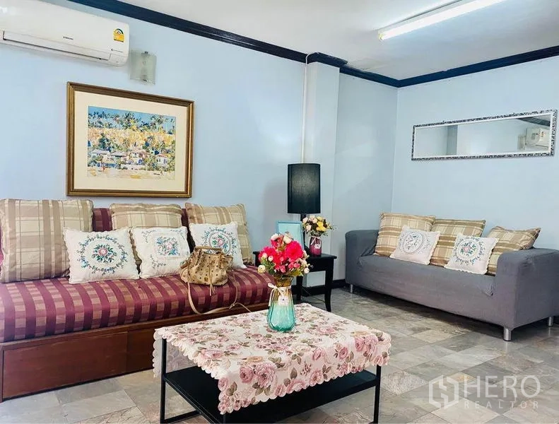 联排别墅 出租或出售在Prawet, Bangkok - 舒适会客区，沙发、空调、墙面装饰与花卉茶几。